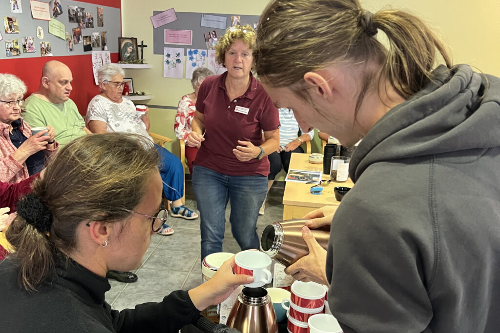 Eine Gruppe von älteren Menschen wird mit Kaffee versorgt. Ein Mann gießt Kaffee in eine Tasse.